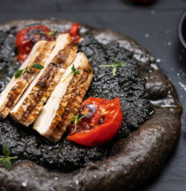 Sort surdeigspizza med skivet kyllingfilet og sort oliventapenade