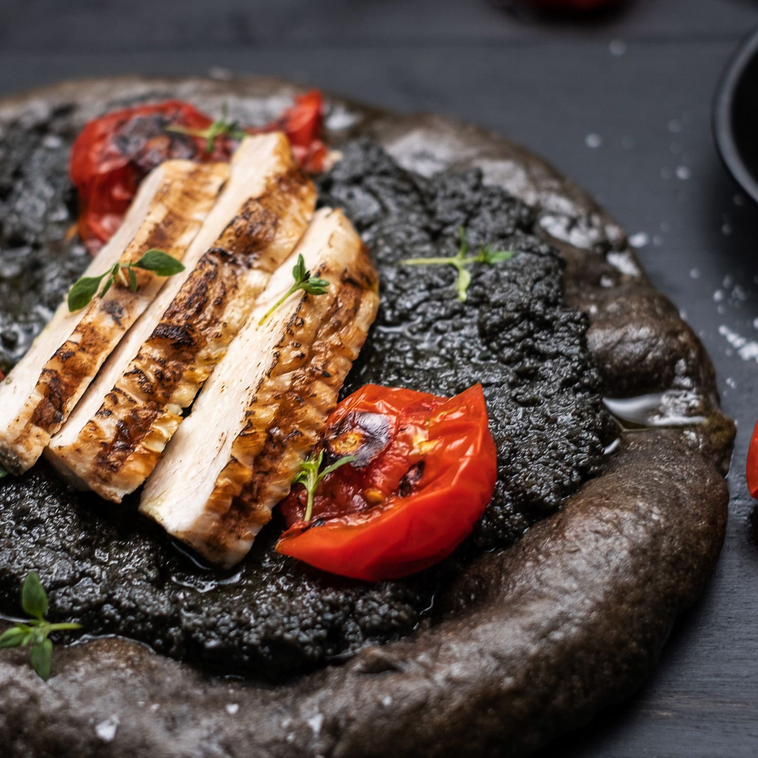 Sort surdeigspizza med skivet kyllingfilet og sort oliventapenade